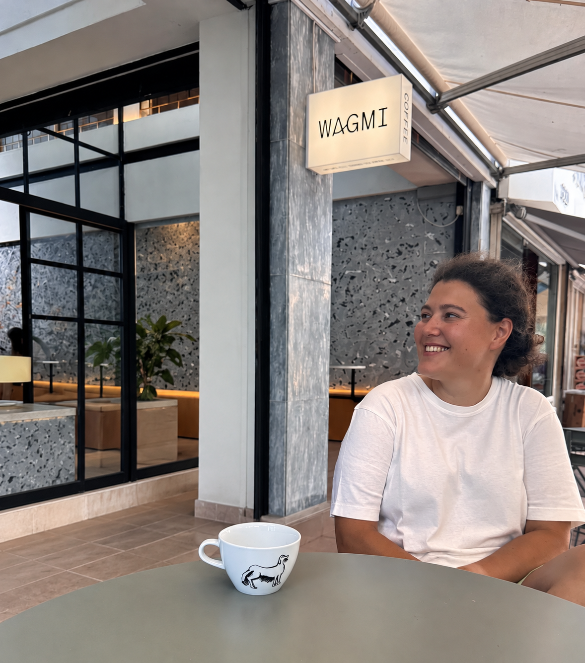 A man and a woman are looking to each other smiling. They are sitting at a table where there is a cup.